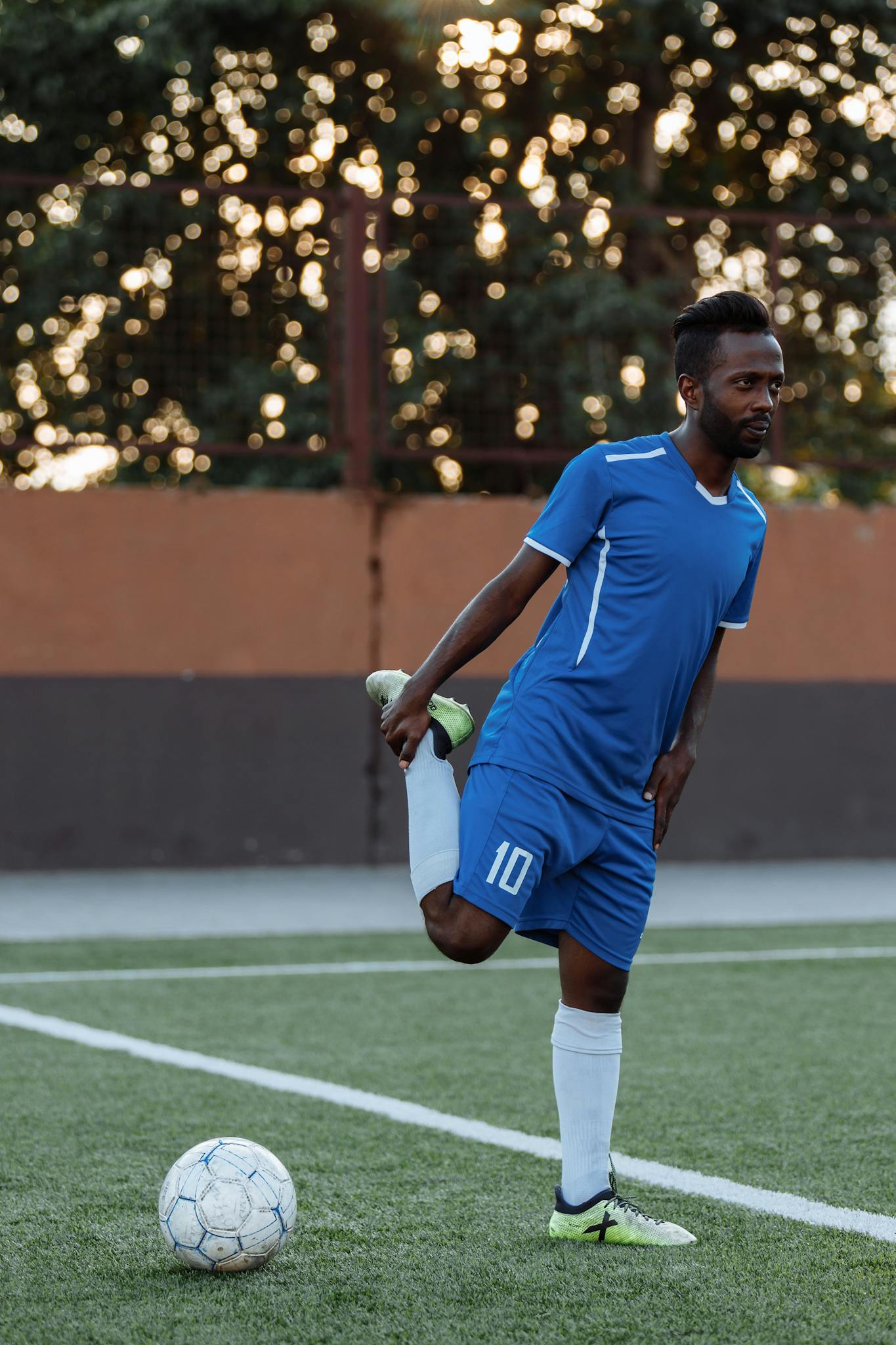 Soccer player in blue uniform stretching on a field with a ball nearby.